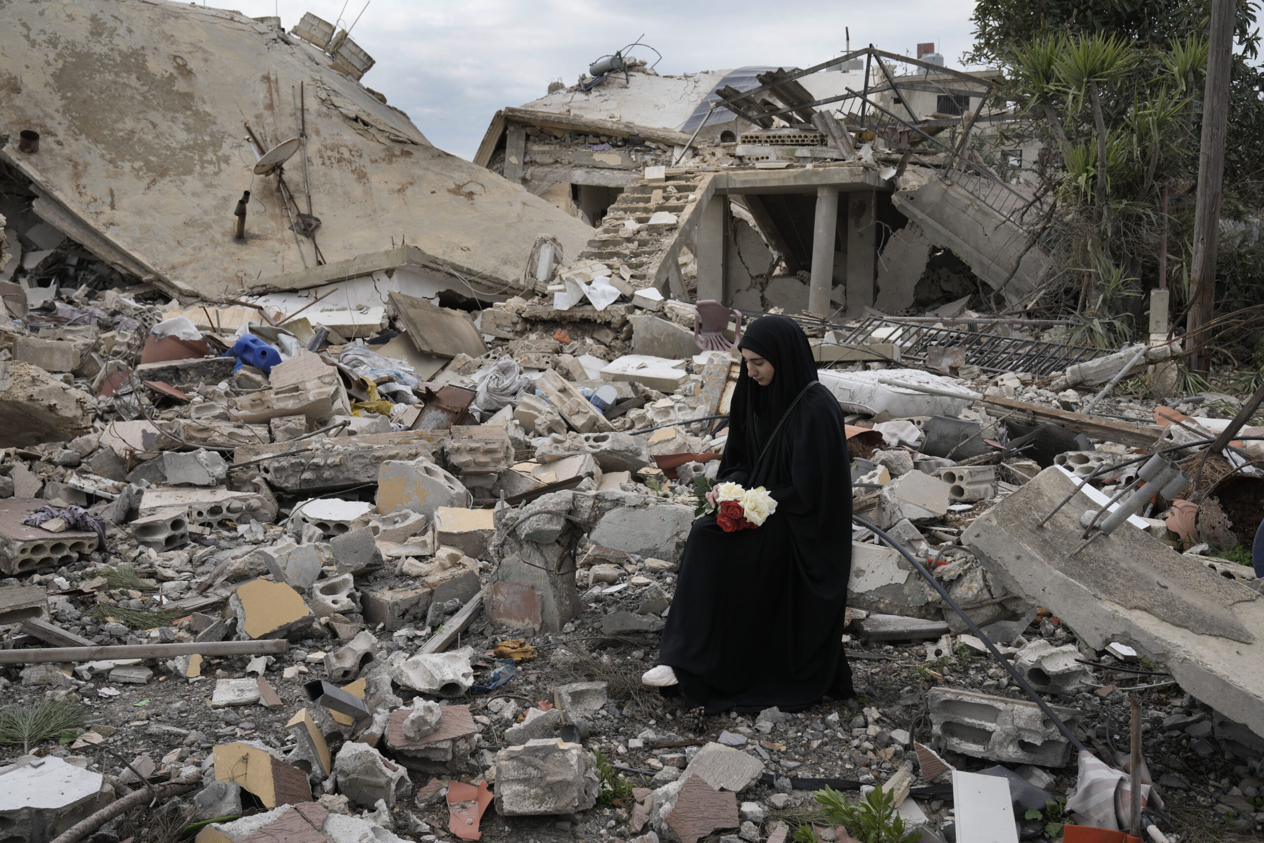 Una mujer libanesa sostiene un ramo de flores mientras permanece sentada entre los escombro de una casa destruida tras una ofensiva aérea y terrestre de Israel. Foto: AP.