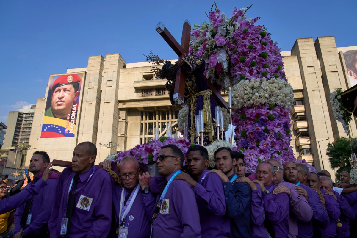 Devotos cargan un paso con la imagen de Jesús, delante de un cartel con la imagen del difunto expresidente Hugo Chávez, durante la procesión del Nazareno de San Pablo, en Caracas, Venezuela